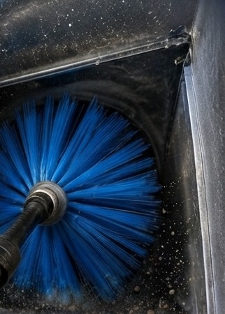 Close-up of a rotary brush agitating dust inside an AC duct